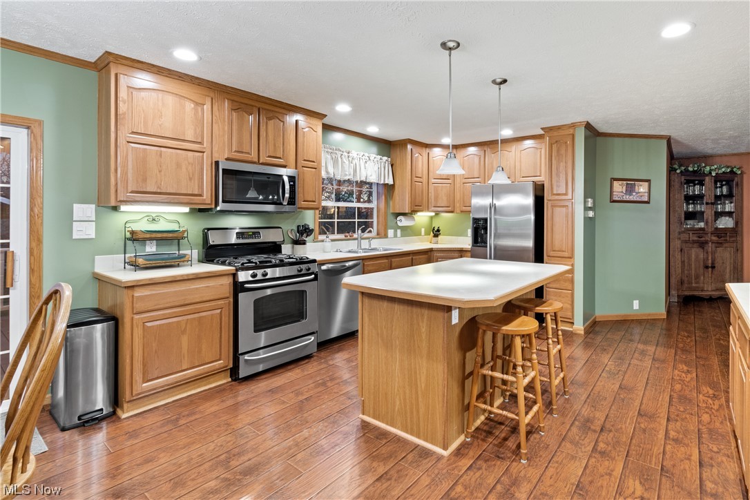 2240 Prysi Road Northwest Dover, OH 44622 - Photo 11 of 35 Kitchen featuring hanging light fixtures, a center island, hardwood / wood-style flooring, a breakfast bar, and stainless steel appliances