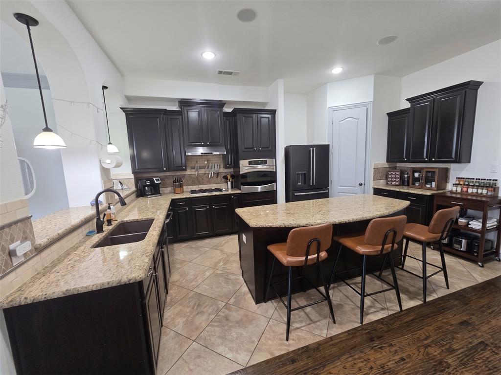 809 Rockingham Drive Irving, TX 75063 - Photo 1 of 30 Dark wood-finish cabinetry, light granite countertops, stainless steel appliances, a center island with bar seating, and tile flooring