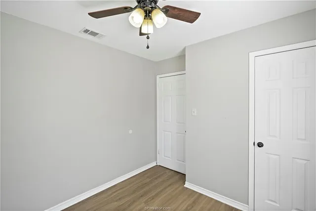 an empty room with a chandelier fan and wooden floor