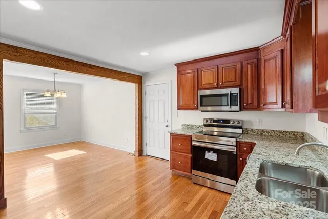 a kitchen with stainless steel appliances granite countertop a stove top oven a sink dishwasher and wooden cabinets with wooden floor