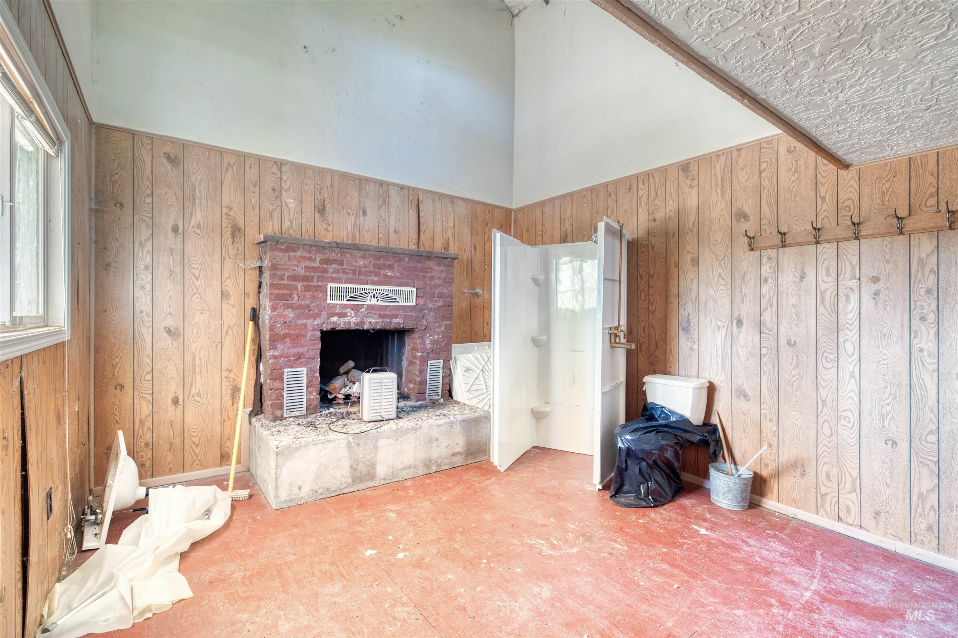 175 Ranft Road Placerville, ID 83666 - Photo 13 of 28 Unfurnished living room featuring wooden walls, a brick fireplace, and a high ceiling