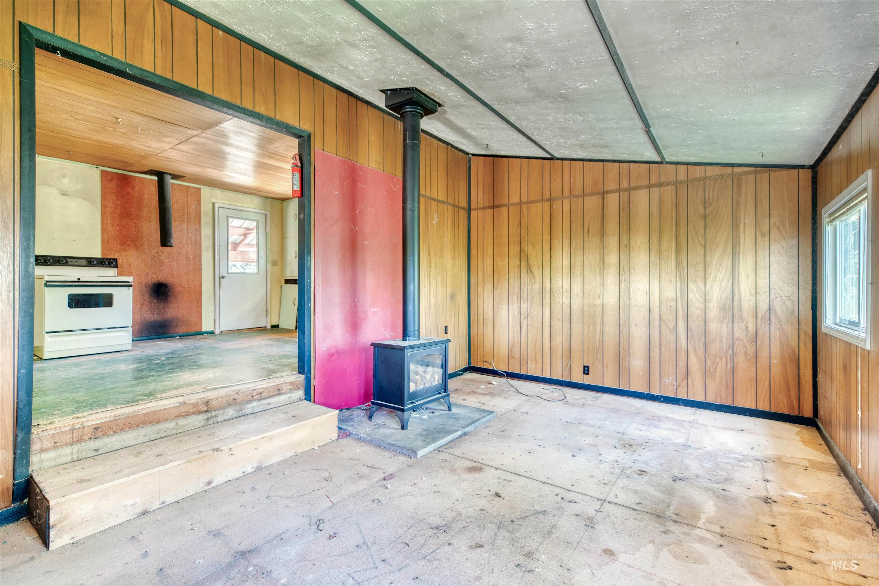 175 Ranft Road Placerville, ID 83666 - Photo 7 of 28 Empty room with a wood stove, wooden walls, and plenty of natural light