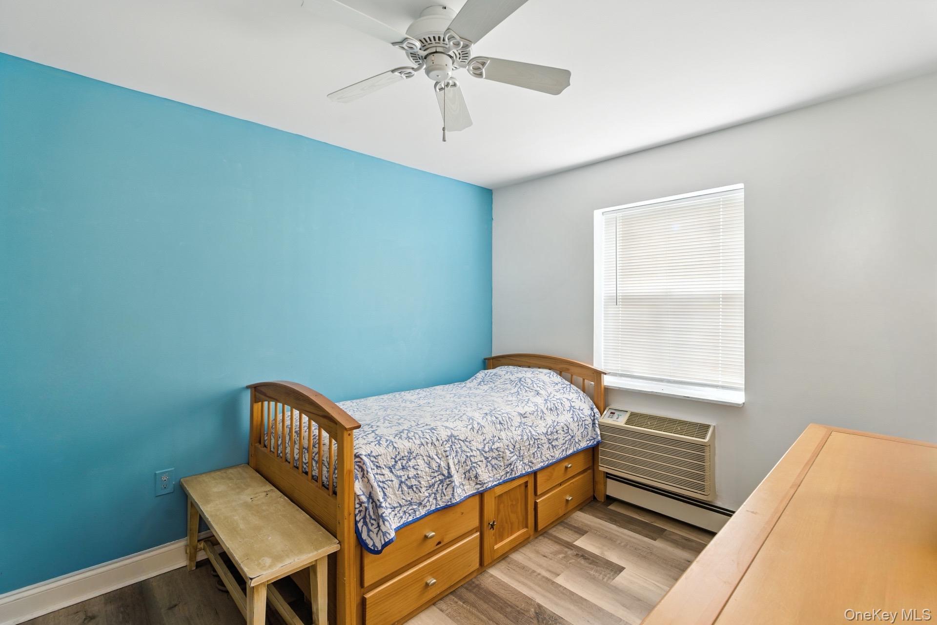 1-76 Beach 101st Street, Unit 4A Queens, NY 11694 - Photo 8 of 16 Bedroom with ceiling fan, wood finished floors, a baseboard radiator, and a wall mounted air conditioner