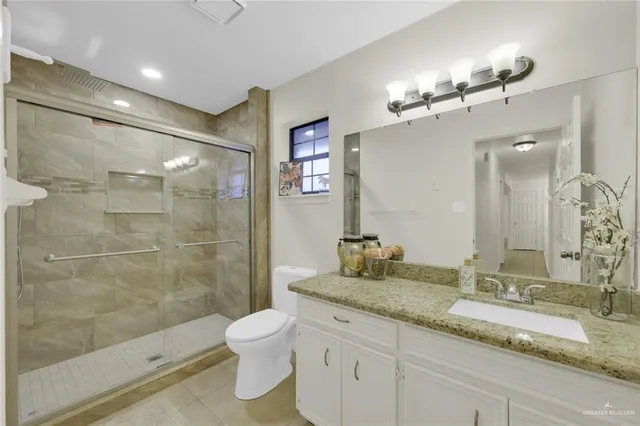 a bathroom with a granite countertop sink a toilet a mirror and shower