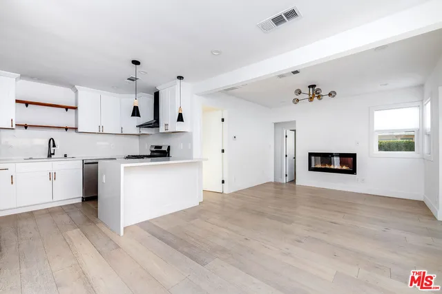 a large white kitchen with granite countertop a stove top oven a sink dishwasher and white cabinets with wooden floor