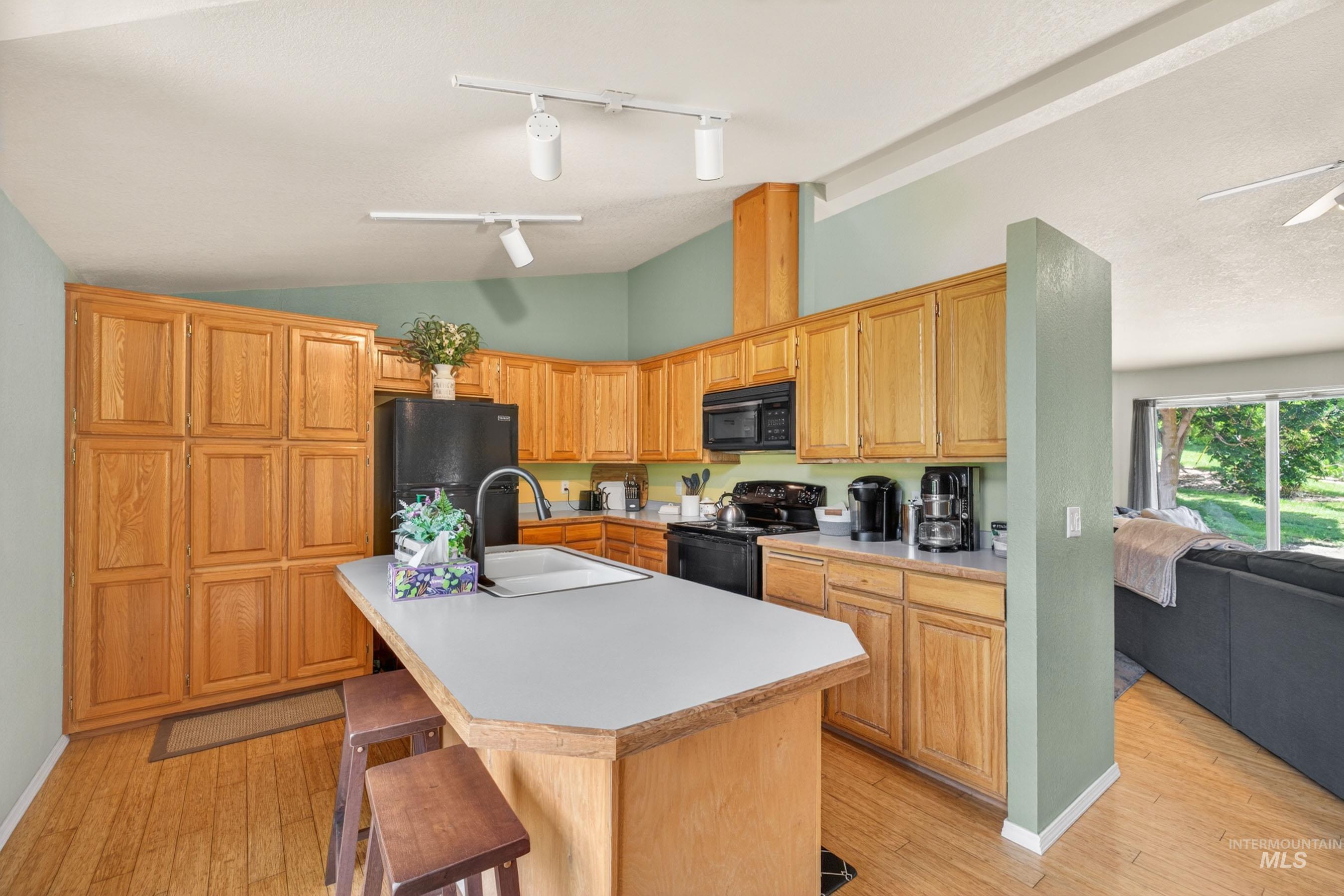 151 Cow Creek Road Lucile, ID 83542 - Photo 17 of 50 Kitchen featuring wood-finish cabinetry, a central island with an integrated sink, black appliances, and track lighting