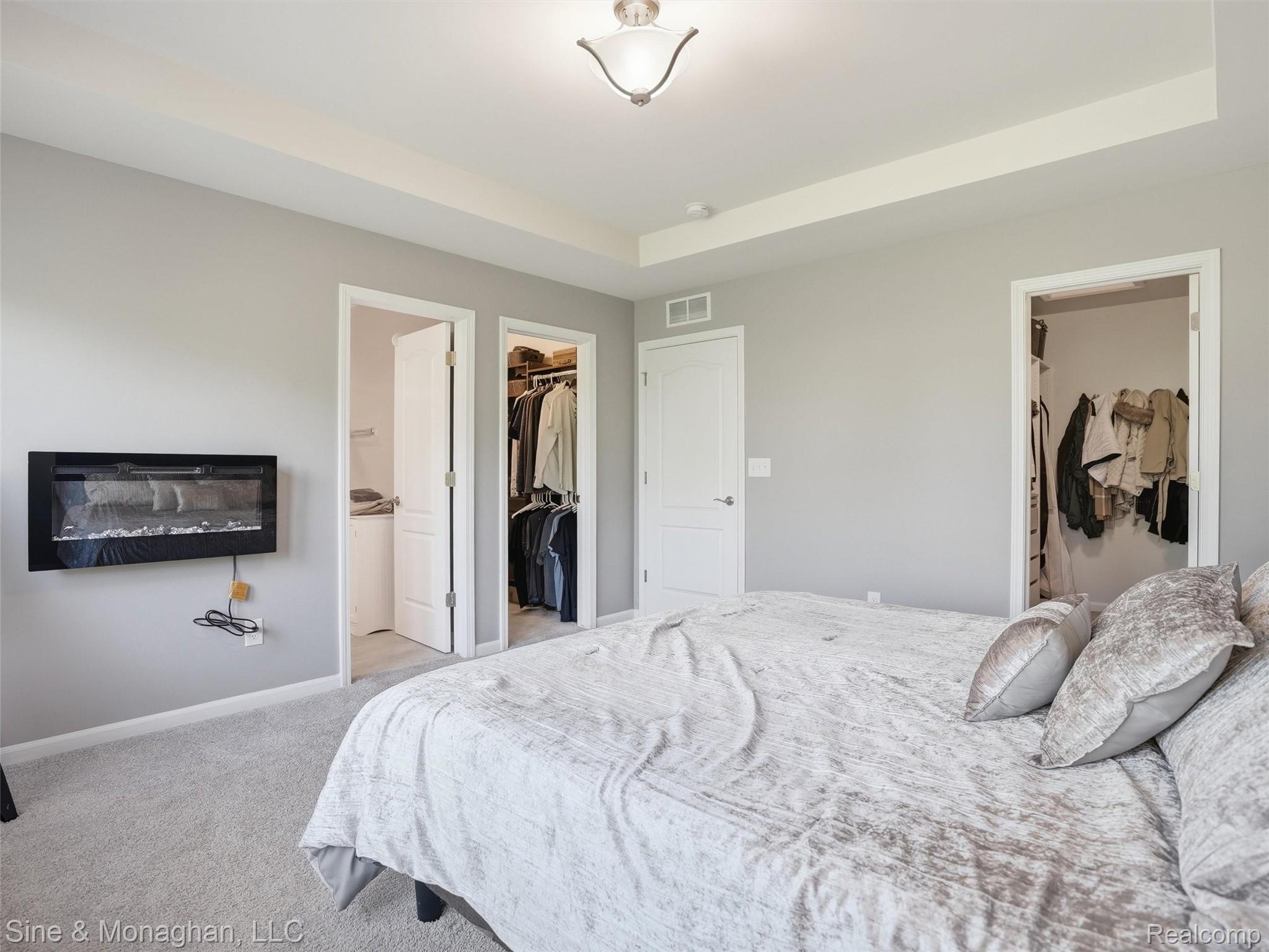 24827 Ivy Road Novi, MI 48375 - Photo 18 of 38 Bedroom featuring a wall-mounted electric fireplace, tray ceiling, and light-colored carpeting