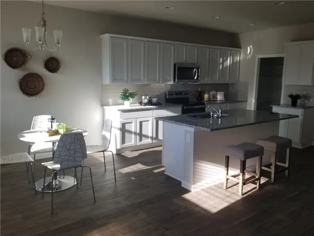 a kitchen with stainless steel appliances granite countertop a stove top oven a sink dishwasher and a dining table with wooden floor