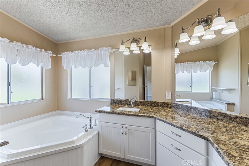 33105 Santiago Road, Unit 149 Acton, CA 93510 - Photo 25 of 28 a bathroom with a granite countertop sink a large mirror and a bathtub with shower