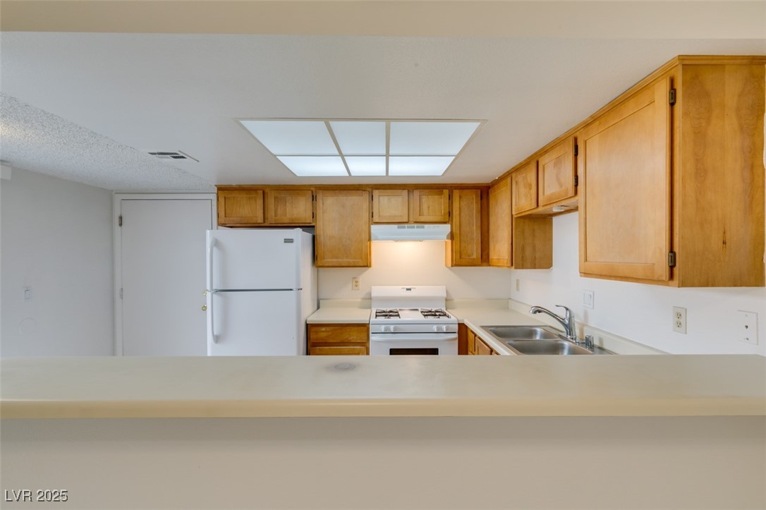2681 Ruthe Duarte Avenue Las Vegas, NV 89121 - Photo 22 of 43 Kitchen with white appliances, visible vents, under cabinet range hood, light countertops, and a sink