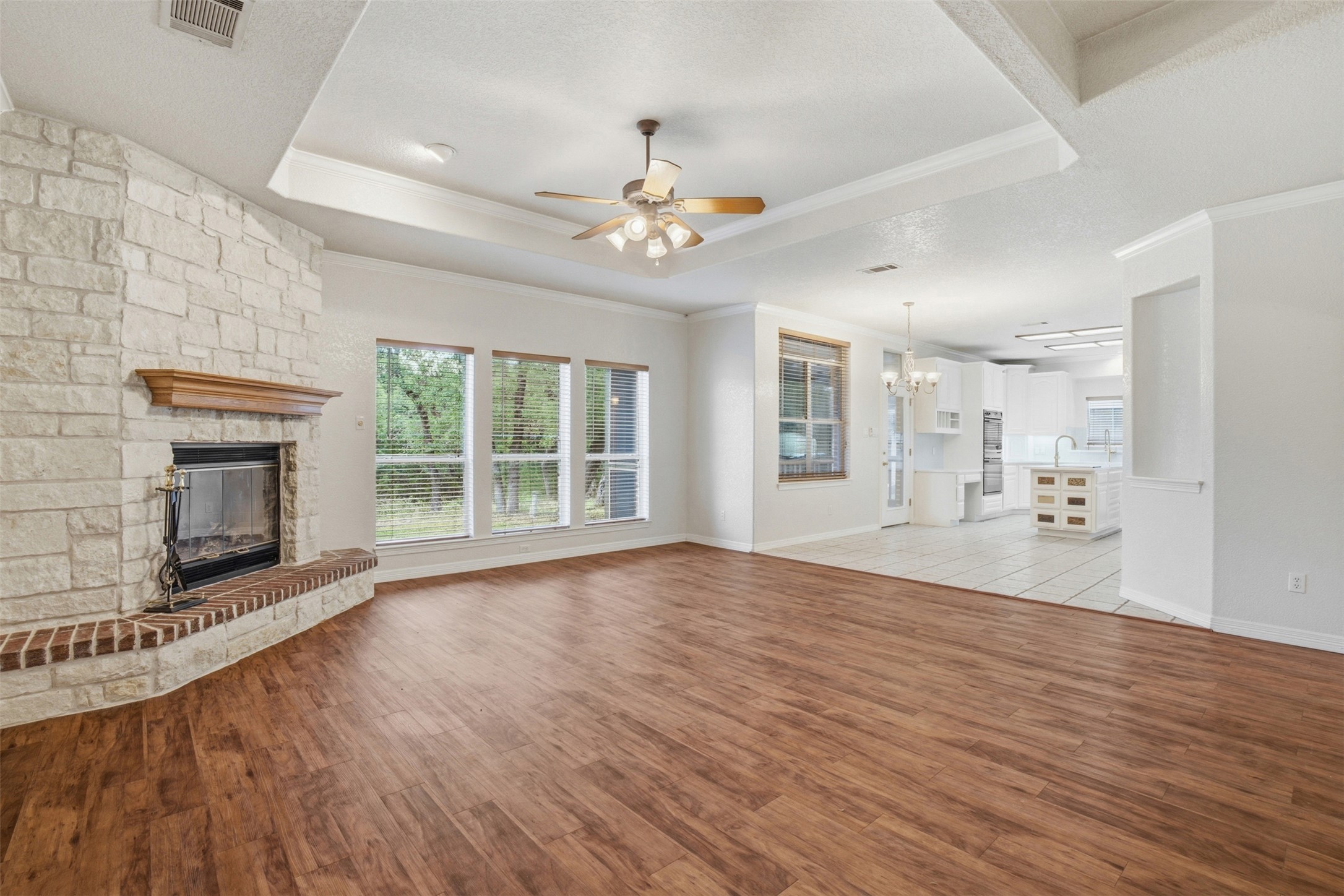 1301 County Road 262 Georgetown, TX 78633 - Photo 11 of 39 Spacious living area featuring wood-finish flooring, a white stone fireplace with brick hearth, multiple windows, and a tray ceiling