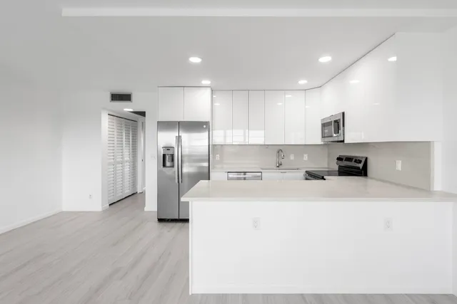 a large white kitchen with a refrigerator a sink dishwasher and a stove with wooden floor