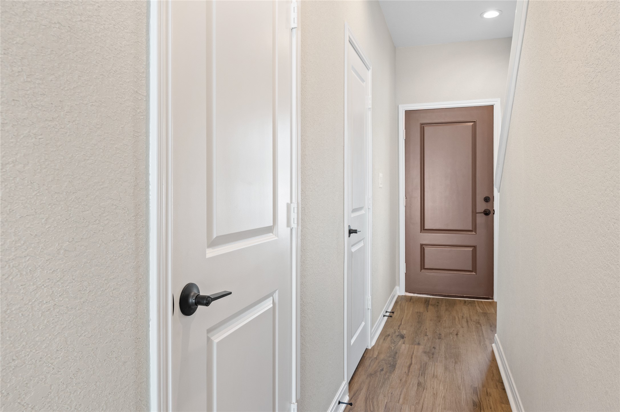 14010 Longstreet Road, Unit 2 Willis, TX 77318 - Photo 27 of 29 This photo shows a bright, narrow hallway, wood flooring, and two doors. It's well-lit with recessed lighting, creating a welcoming entryway.