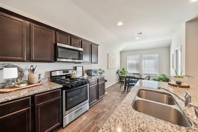 a kitchen with granite countertop a sink a stove top oven and wooden cabinetry