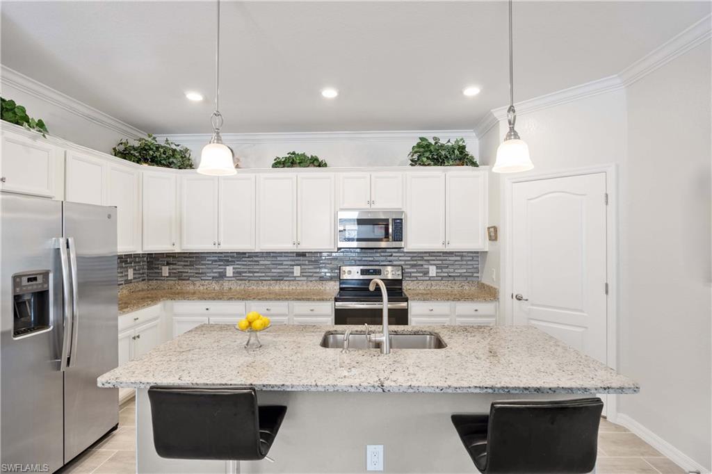 1602 Santiago Circle Naples, FL 34113 - Photo 15 of 49 Kitchen with stainless steel appliances, white cabinetry, decorative backsplash, a kitchen breakfast bar, and an island with sink