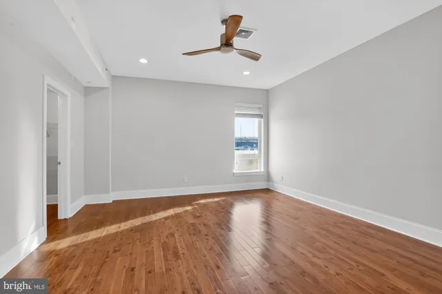 a view of empty room with wooden floor and fan