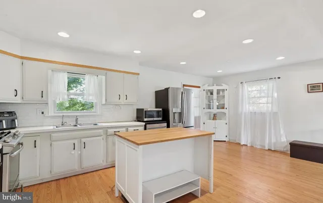 a kitchen with stainless steel appliances a stove a sink dishwasher a refrigerator with white cabinets and wooden floor