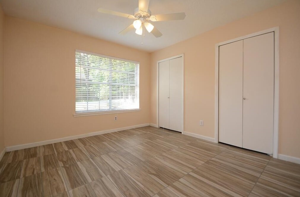 15 South Tallowberry Drive Spring, TX 77381 - Photo 16 of 26 Room with soft peach walls, light tile flooring, two white closets, a ceiling fan, and a large window with blinds for natural light.