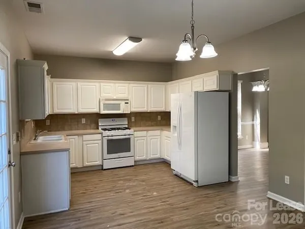 a kitchen with stainless steel appliances granite countertop a refrigerator a sink dishwasher a stove and white cabinets with wooden floor