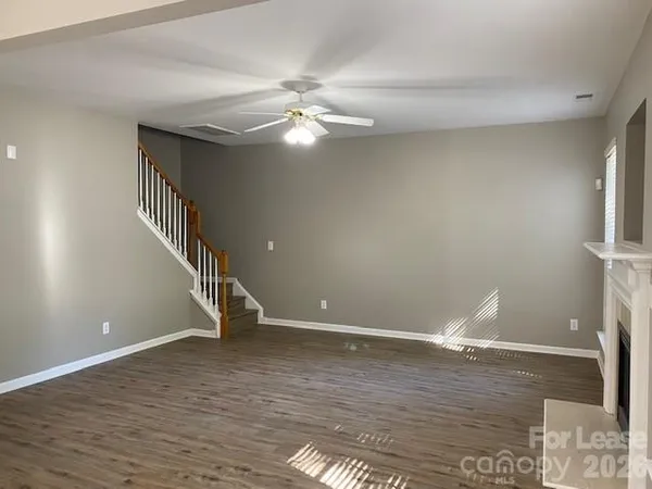 a view of an empty room with wooden floor and a ceiling fan