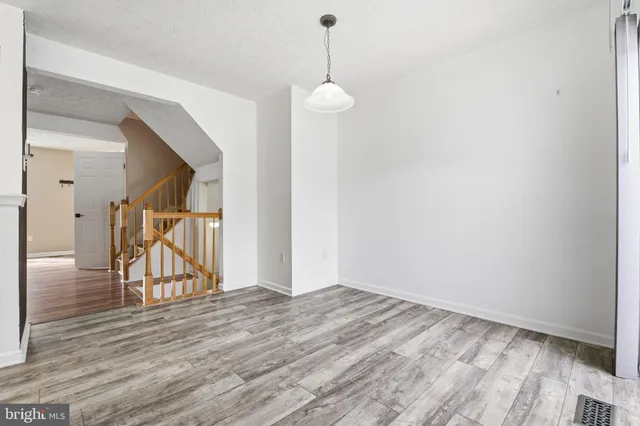 a view of an empty room with wooden floor and a hallway