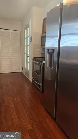 a view of a refrigerator in kitchen and an empty room with wooden floor