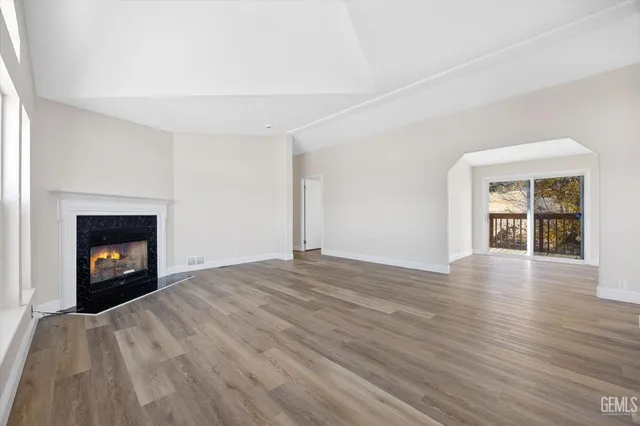 an empty room with wooden floor fire place and windows