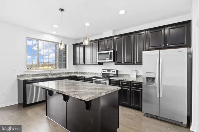 a kitchen with kitchen island granite countertop stainless steel appliances a sink stove refrigerator and a window