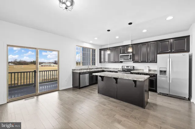 a kitchen with stainless steel appliances granite countertop a refrigerator a sink dishwasher a oven and a large countertops with wooden floor