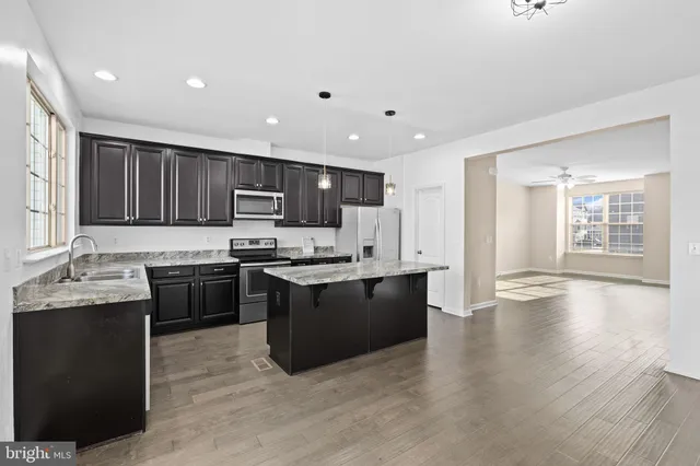 a kitchen with stainless steel appliances granite countertop wooden cabinets a refrigerator a sink a stove a microwave and wooden floors