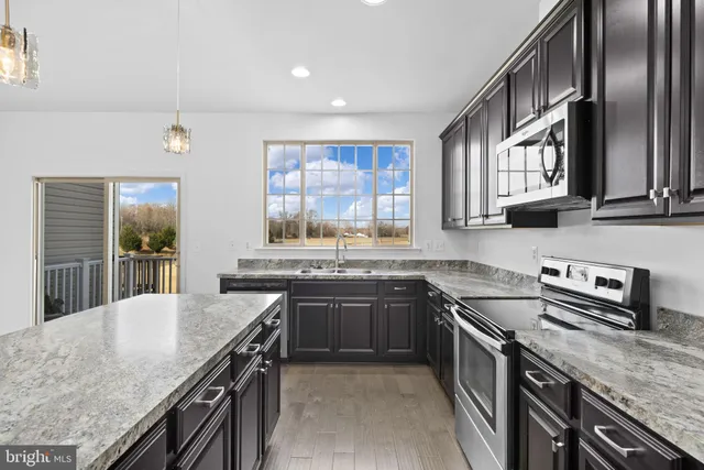 a kitchen with stainless steel appliances granite countertop stove a sink dishwasher a refrigerator and wooden cabinets with wooden floor