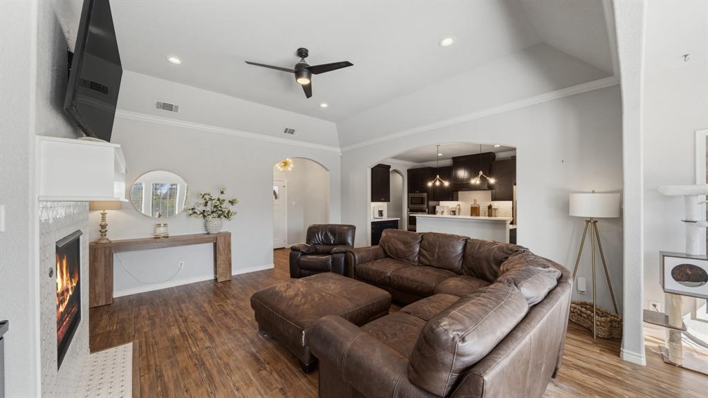 101 Lighthouse Lane Mabank, TX 75143 - Photo 6 of 40 Living area featuring a warm lit fireplace, crown molding, dark wood-style floors, a ceiling fan, and arched walkways