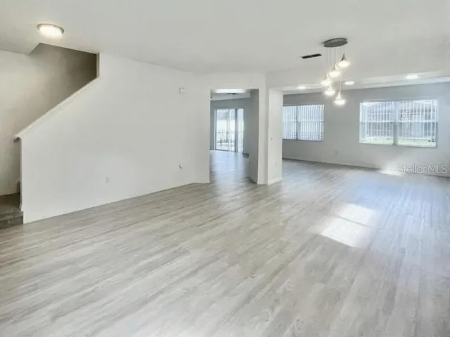 a view of an empty room with wooden floor and a ceiling fan