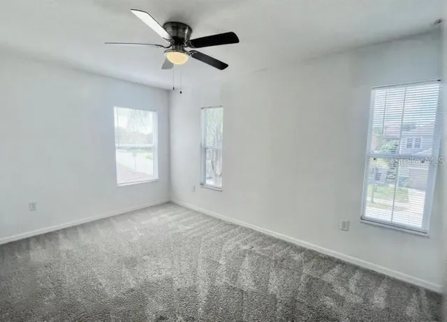 an empty room with windows and ceiling fan