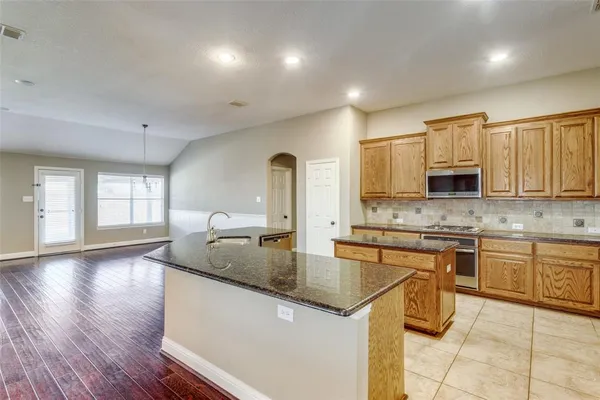 a open kitchen with stainless steel appliances granite countertop a refrigerator a stove a sink dishwasher and a dining table with wooden floor
