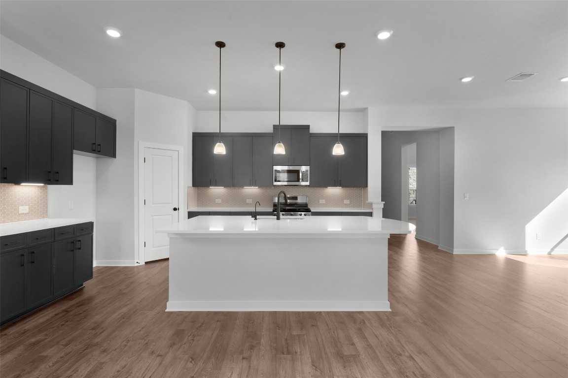 237 Wingstem Way Georgetown, TX 78633 - Photo 8 of 26 Kitchen featuring decorative light fixtures, stainless steel appliances, a center island with sink, dark wood-type flooring, and recessed lighting