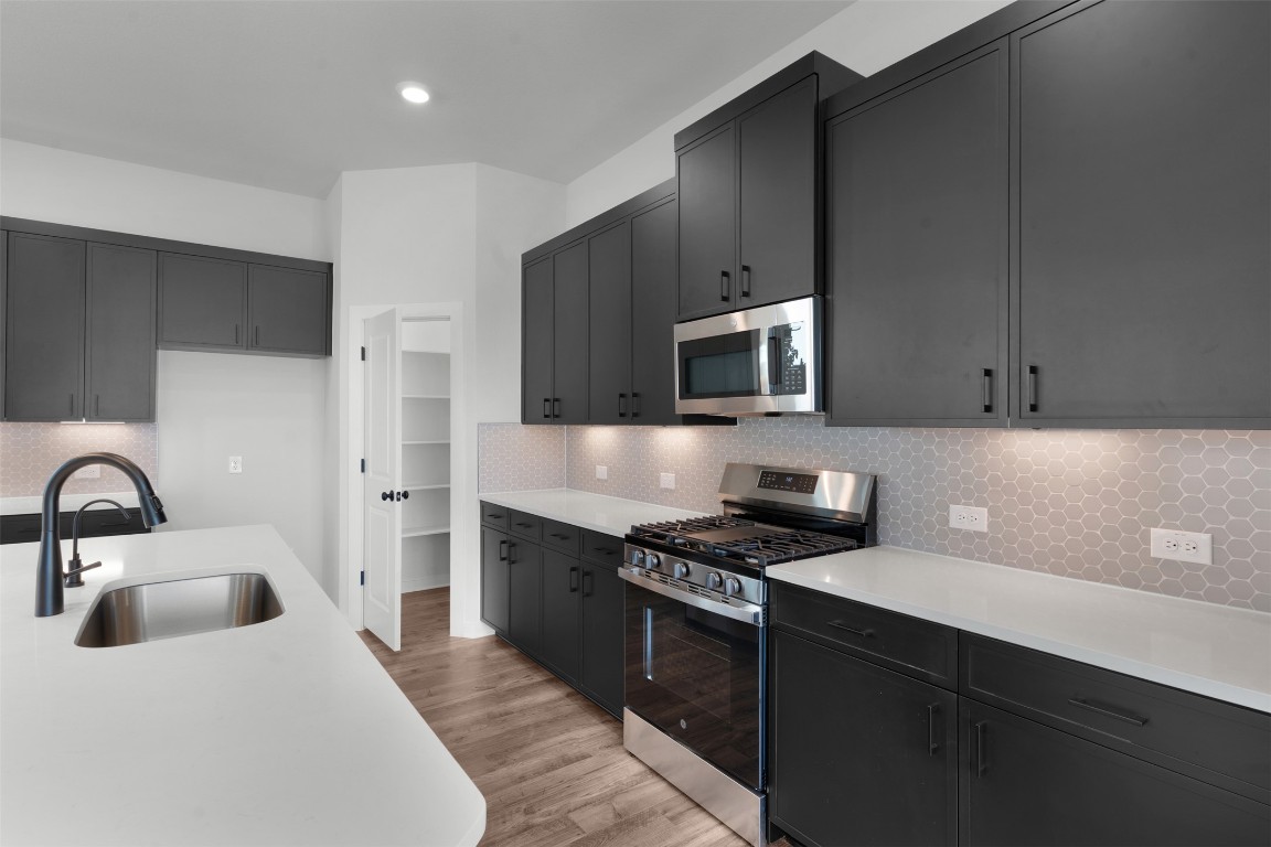 237 Wingstem Way Georgetown, TX 78633 - Photo 9 of 26 Kitchen featuring appliances with stainless steel finishes, light wood finished floors, dark cabinets, light stone countertops, and decorative backsplash