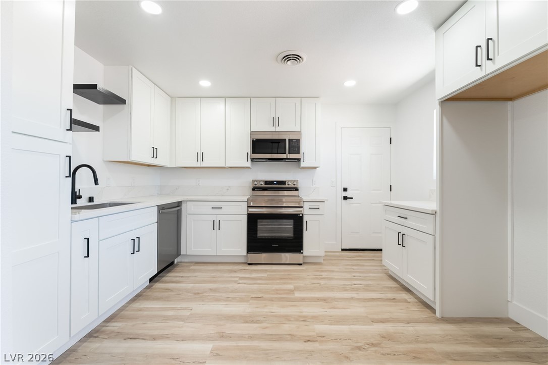 39 Lowery Street Henderson, NV 89015 - Photo 9 of 40 A well-lit kitchen with sleek white cabinetry and elegant light wood flooring.