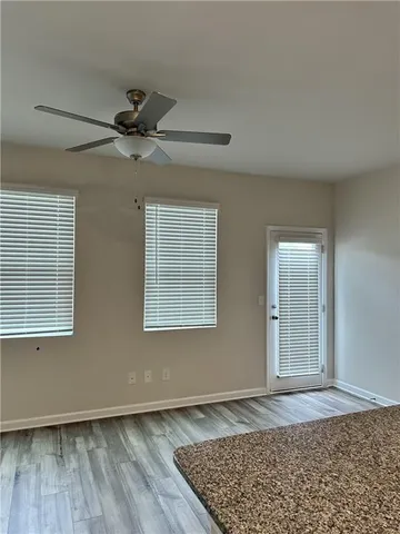 an empty room with wooden floor a ceiling fan and windows