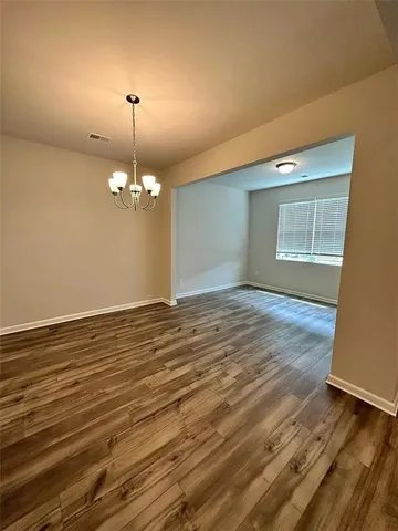 an empty room with wooden floor chandelier and windows