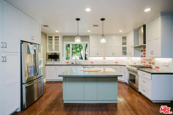 a kitchen with stainless steel appliances granite countertop a refrigerator a sink dishwasher a oven and a dining table with wooden floor