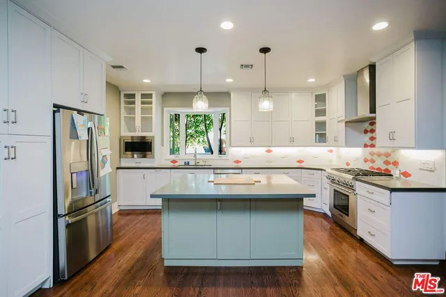 a kitchen with stainless steel appliances granite countertop a refrigerator a sink dishwasher a oven and a dining table with wooden floor