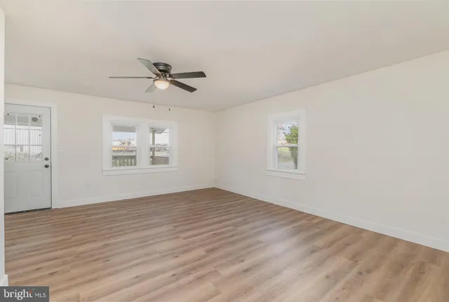 an empty room with wooden floor ceiling fan and windows