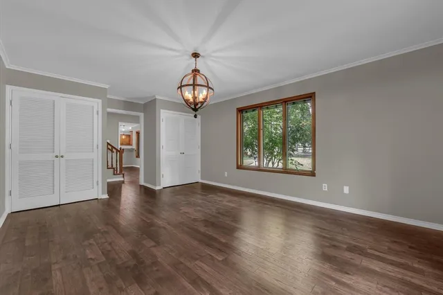 an empty room with wooden floor chandelier and windows