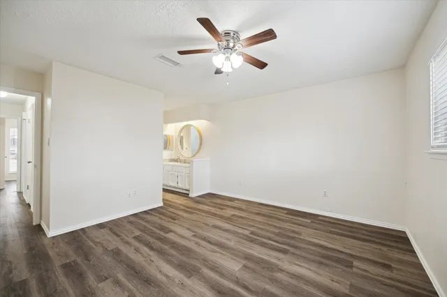 a view of an empty room with wooden floor and a ceiling fan