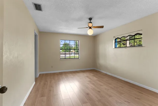 an empty room with wooden floor chandelier fan and windows