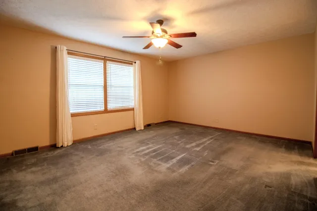 an empty room with a chandelier fan and windows