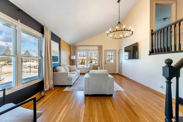 a living room with couches chandelier and a dining table with wooden floor