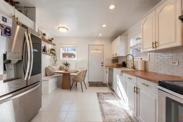 a kitchen with stainless steel appliances granite countertop a refrigerator a sink dishwasher a dining table and chairs with wooden floor