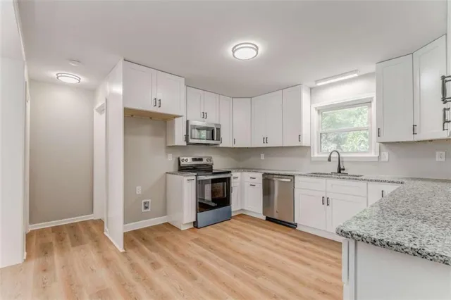 a kitchen with granite countertop a sink stove a refrigerator and white cabinets with wooden floor